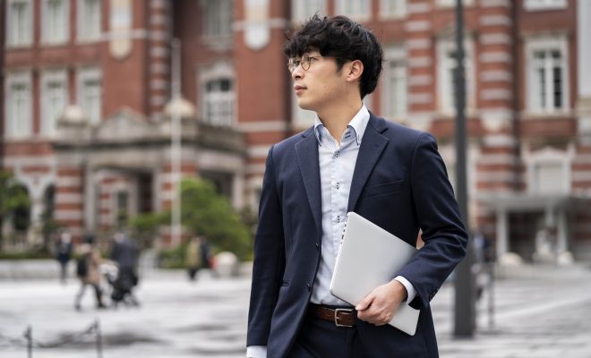 male asian business student in formal wear carrying a laptop